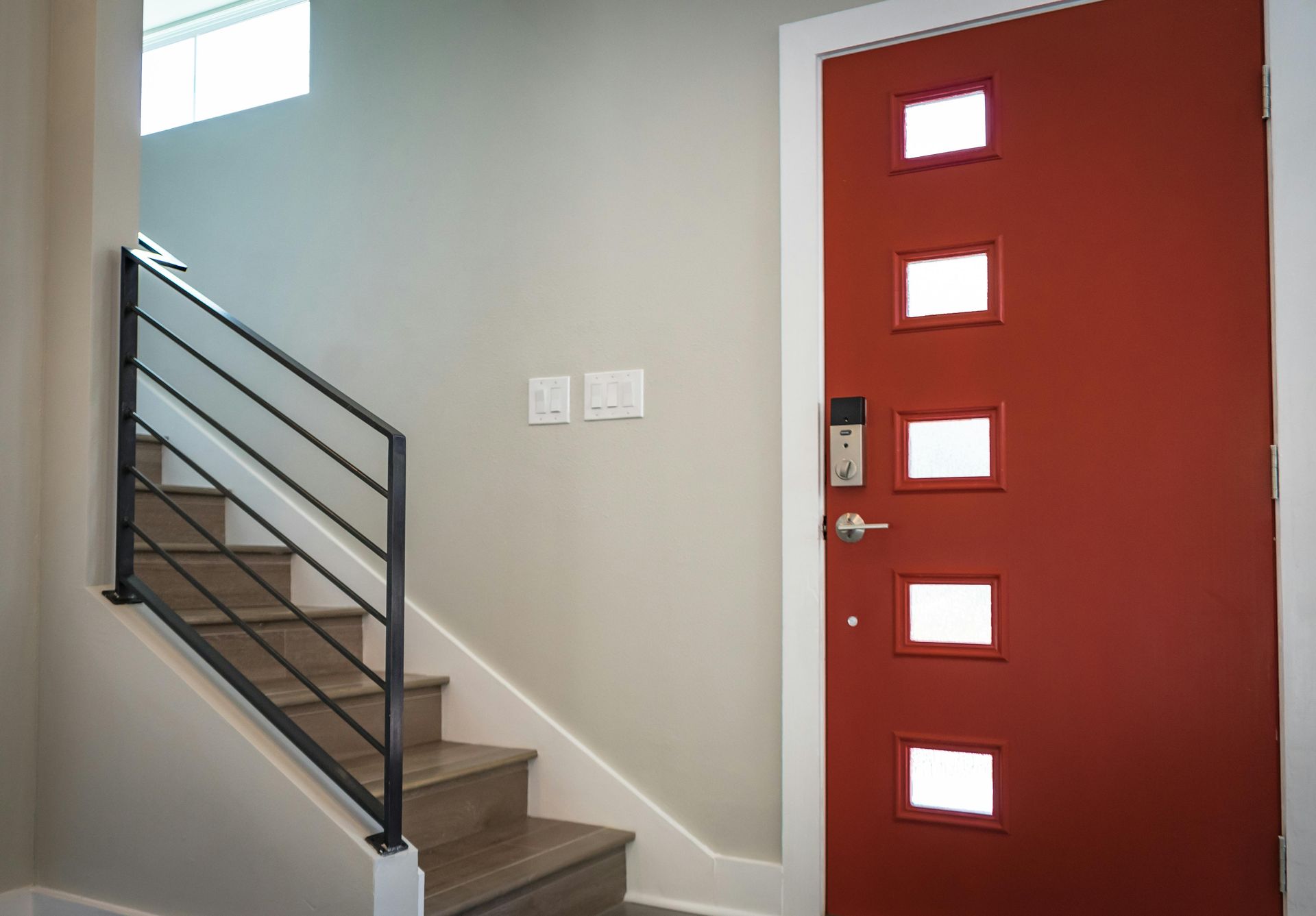 Staircase with black railing and red door with square windows.