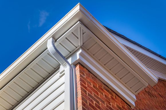 Corner of a building with white trim, gutters, and red brick against a clear blue sky.