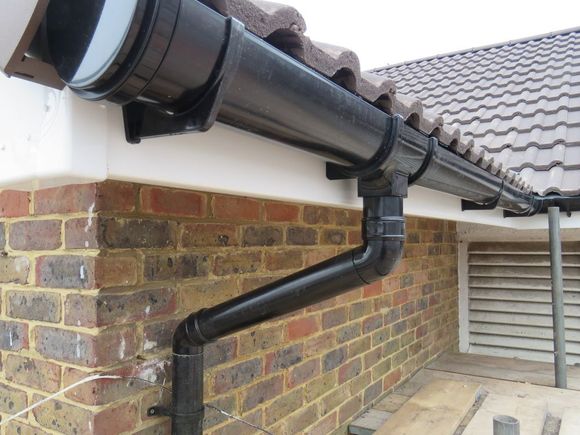 Black rain gutter system on a brick building with gray roof tiles.