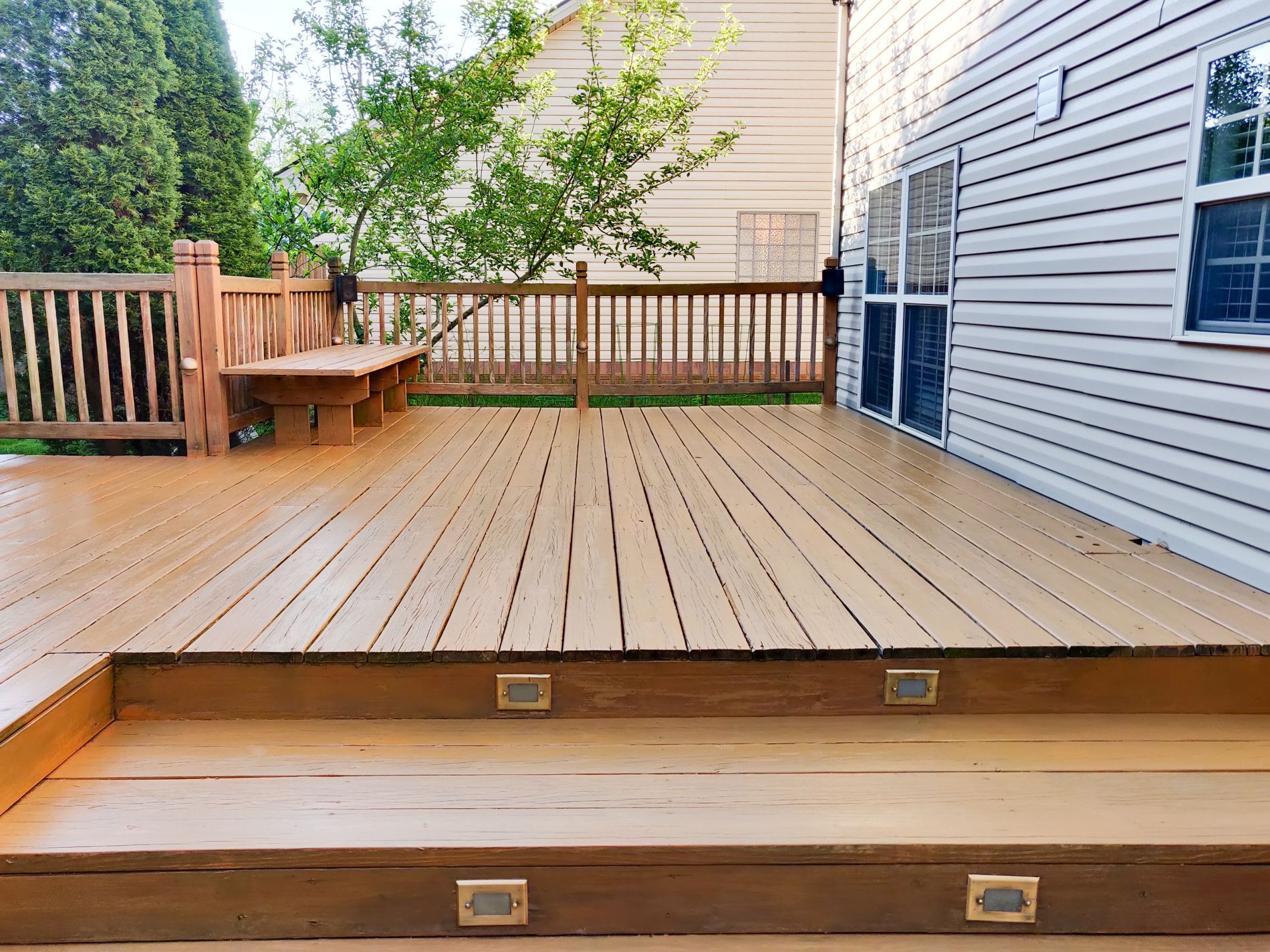 Wooden deck with steps, built-in bench, and railing. Home siding visible.
