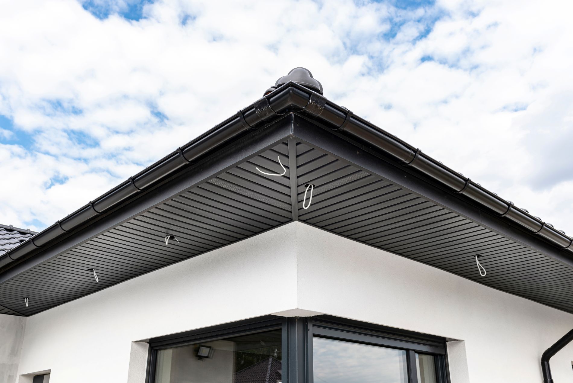 Black-trimmed house corner with dark soffit and cloudy sky.