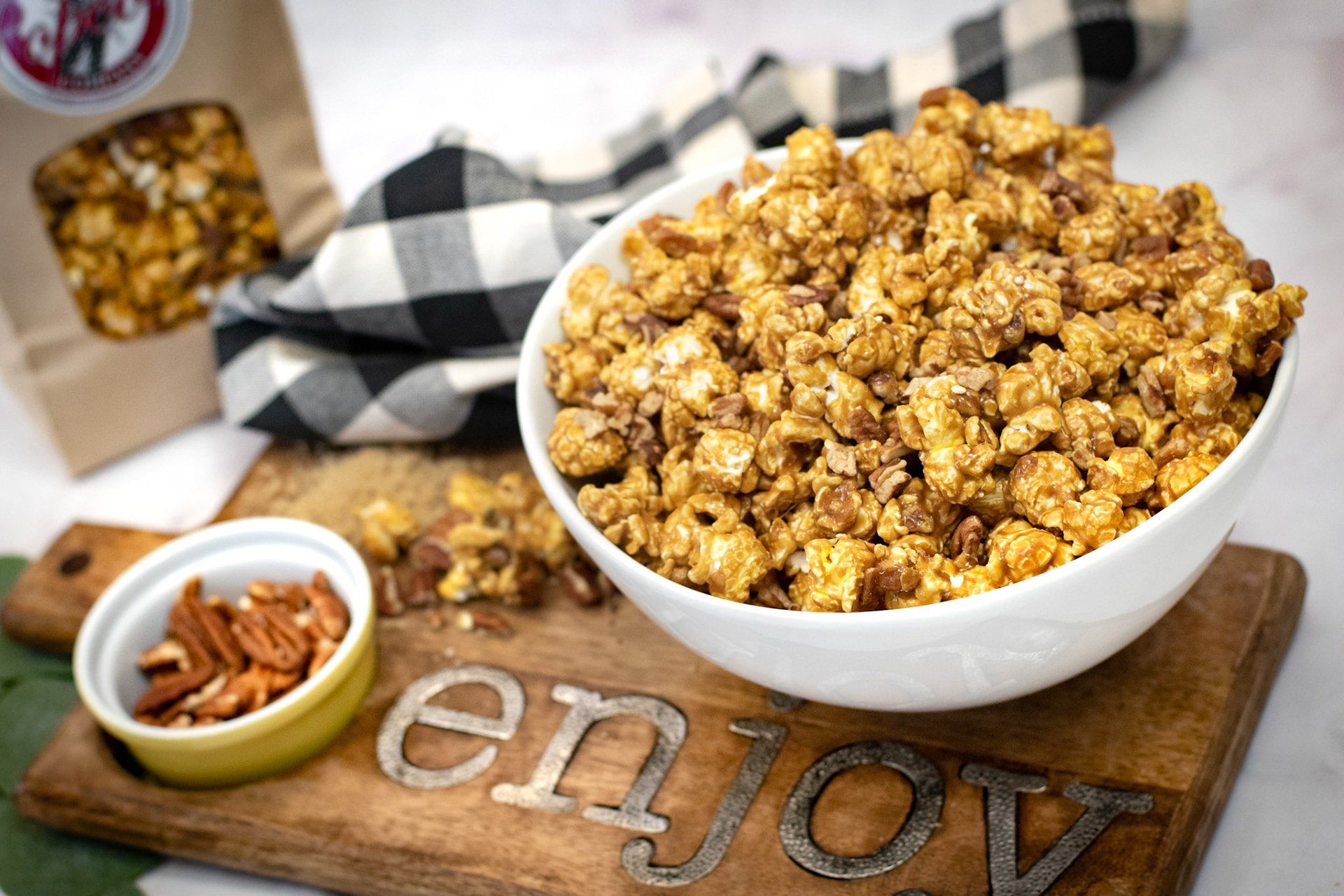 A bowl of caramel popcorn is sitting on a wooden cutting board.