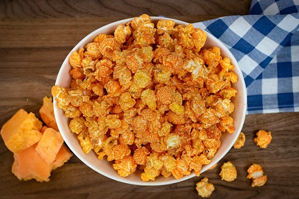 A bowl of cheese popcorn is sitting on a wooden table.
