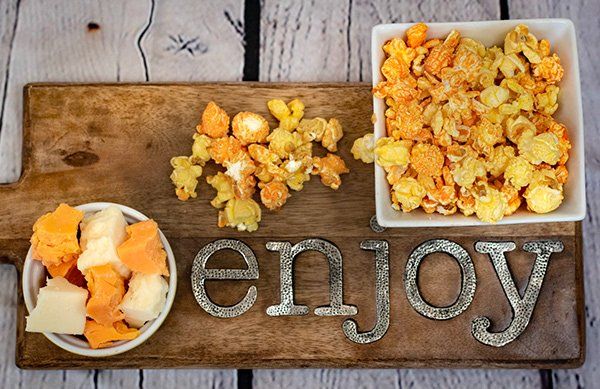 A wooden cutting board with bowls of food and the word enjoy written on it.