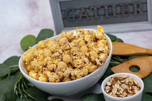 A bowl of caramel popcorn next to a bowl of almonds.
