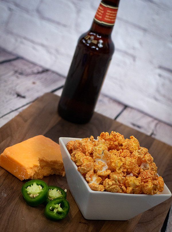 A bowl of popcorn and a bottle of beer on a wooden table.