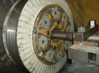 A large machine is sitting in a factory next to a truck.