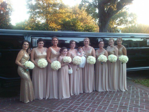 A group of bridesmaids are posing for a picture in front of a limousine.