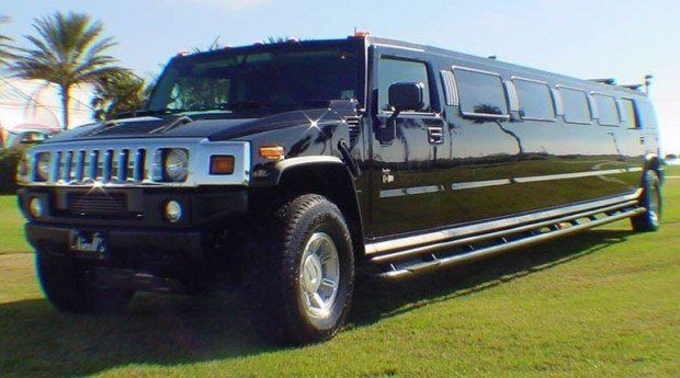 A black hummer limousine is parked in the grass