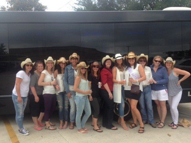A group of women wearing cowboy hats are standing in front of a bus