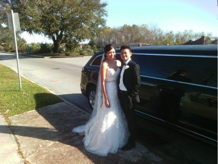 A bride and groom pose in front of a black limousine