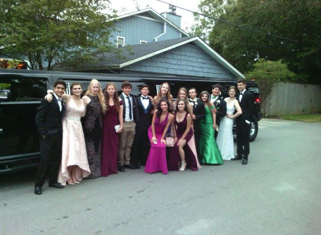 A group of people posing for a picture in front of a limousine