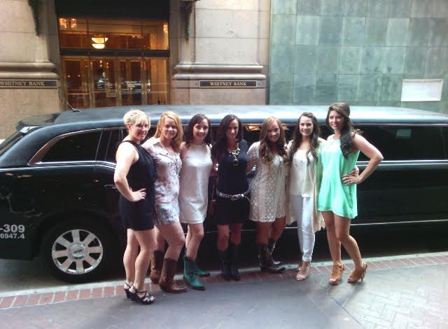 A group of women are posing for a picture in front of a black limousine