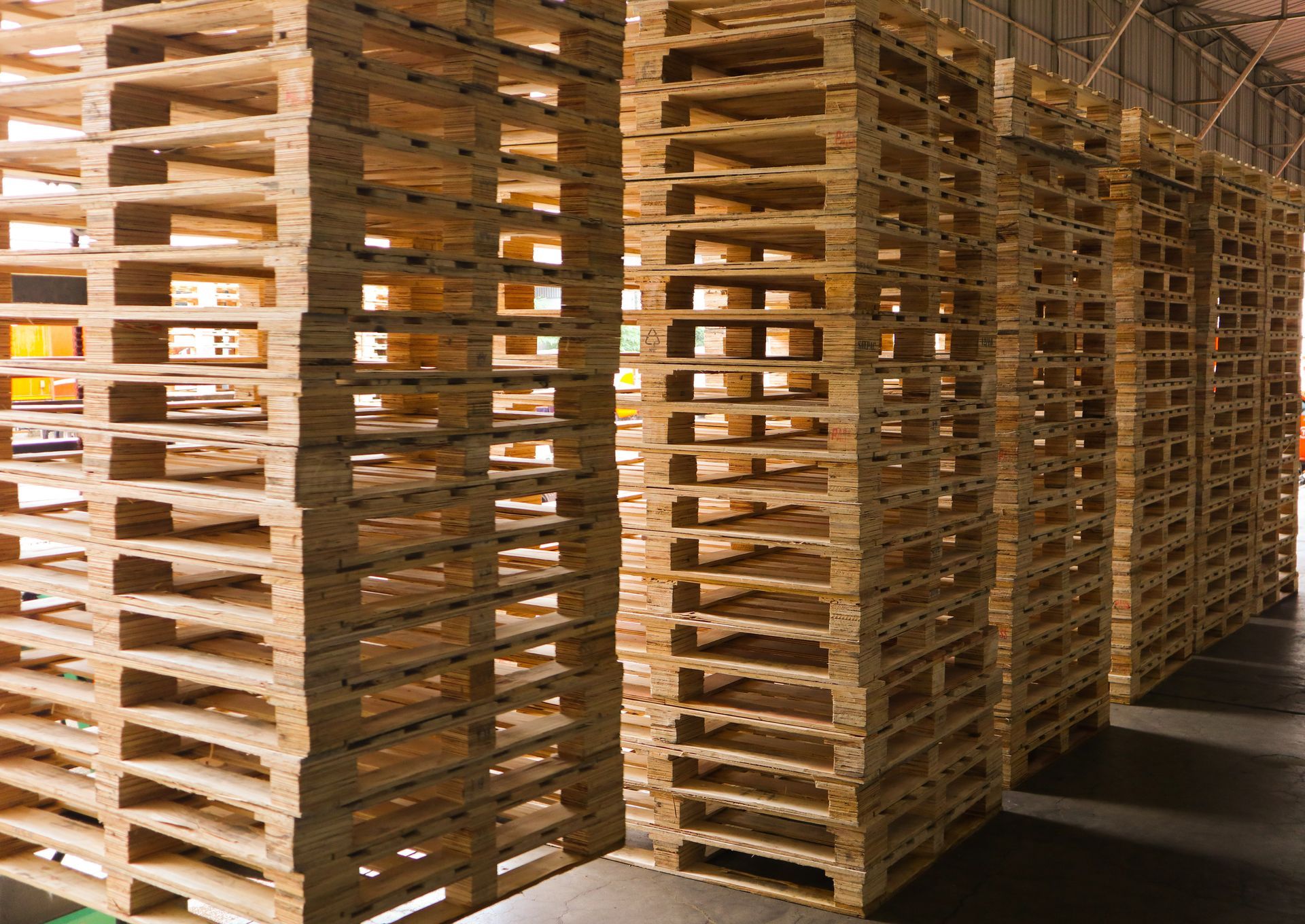 Stacks of light-brown wooden shipping pallets arranged in rows on a concrete floor inside a warehouse.