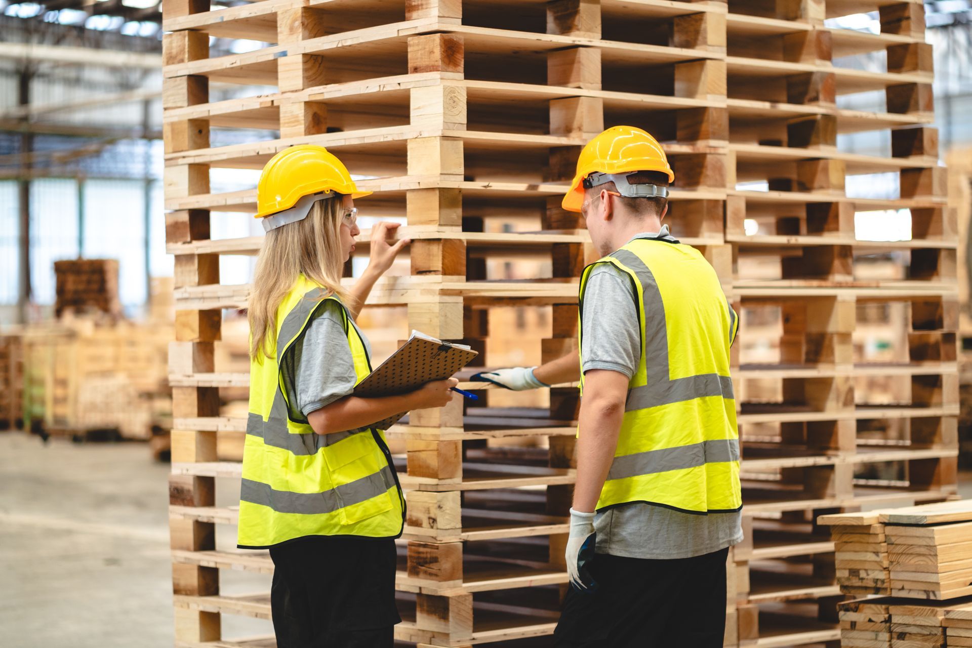 Forklift carrying a stack of wooden pallets in a warehouse.