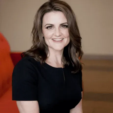 A woman in a black dress is smiling for the camera while sitting on a couch.