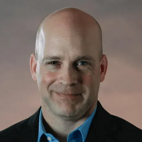 A bald man in a suit and blue shirt is smiling for the camera.