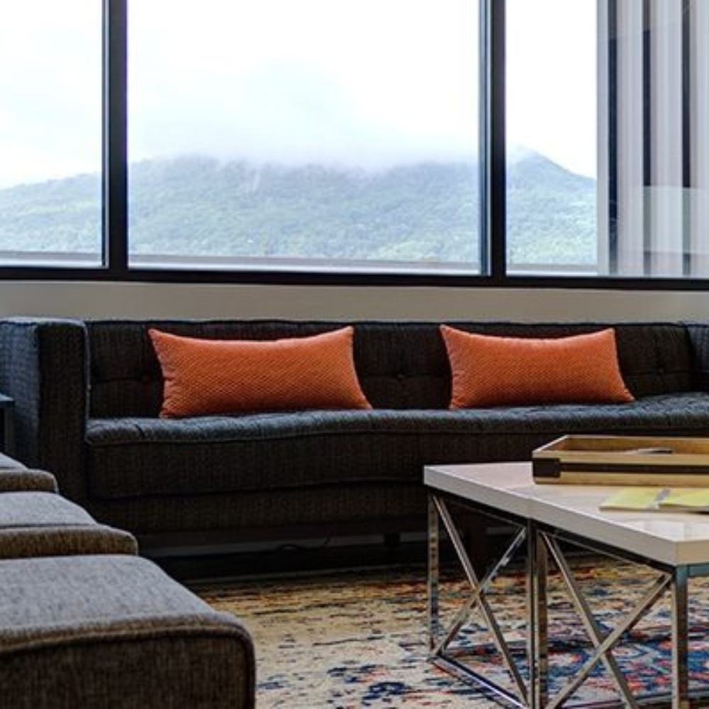 A living room with a couch , coffee table , and large windows.