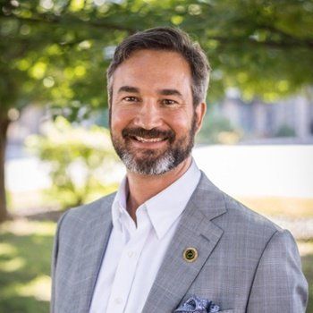 A man with a beard is wearing a suit and smiling for the camera.