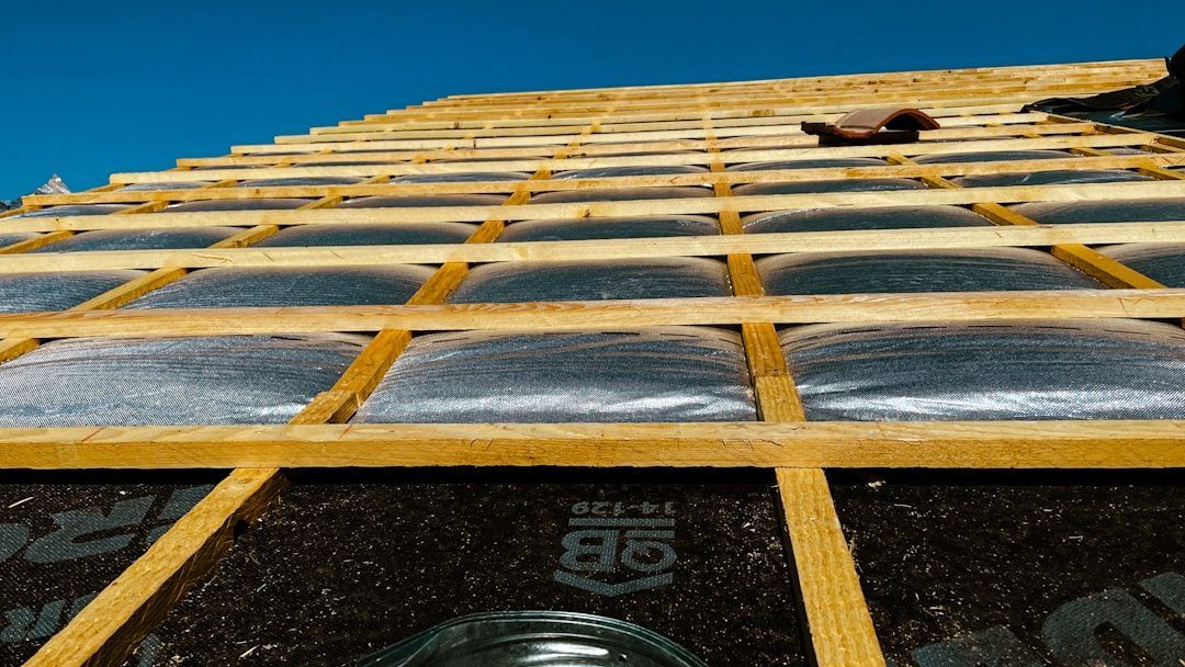 Wooden roof frame with clear sheeting and dark underlayment against a blue sky.