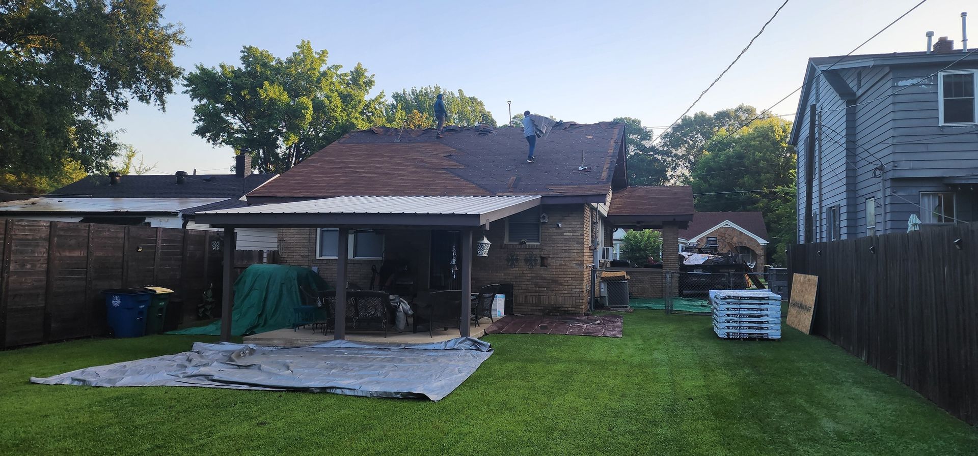 Backyard view of a house with a grass lawn, wooden fence, and trees under a clear blue sky.