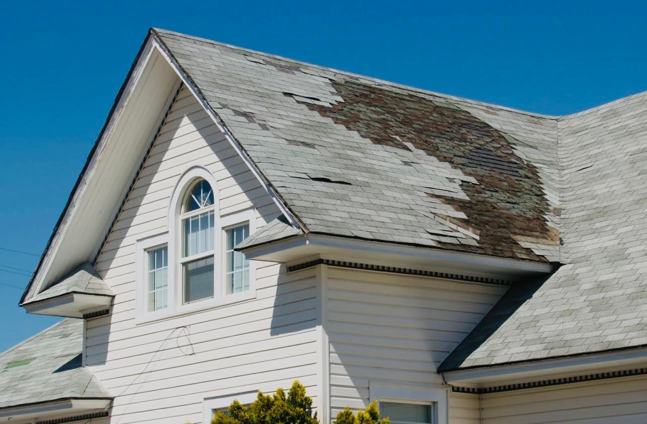 White house with weathered shingles on the roof under a blue sky.