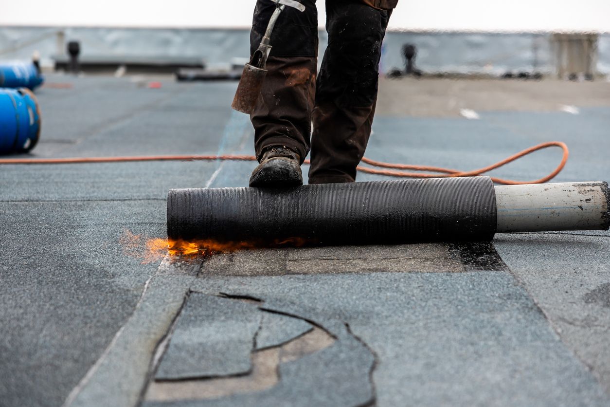 Roofer welding roofing material with a torch on a flat roof.