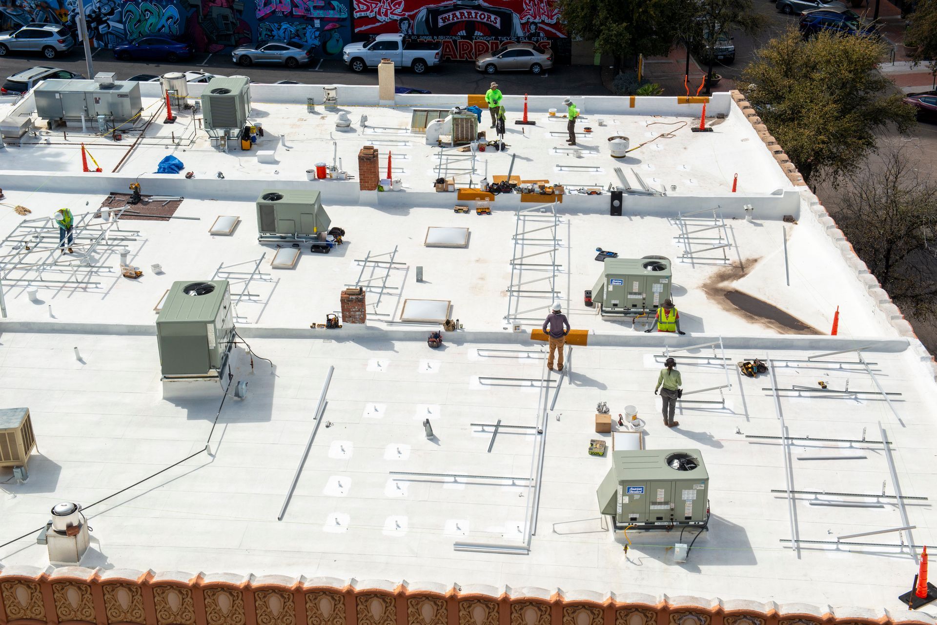 Workers installing equipment on a flat roof. Several workers are present, with construction materials and machinery visible.