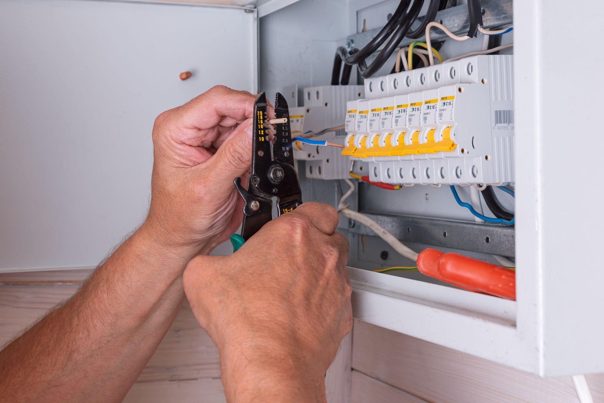 Hands wiring an electrical panel with circuit breakers and tools visible.