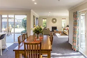A dining room table and chairs in a house with a vase of flowers on it.