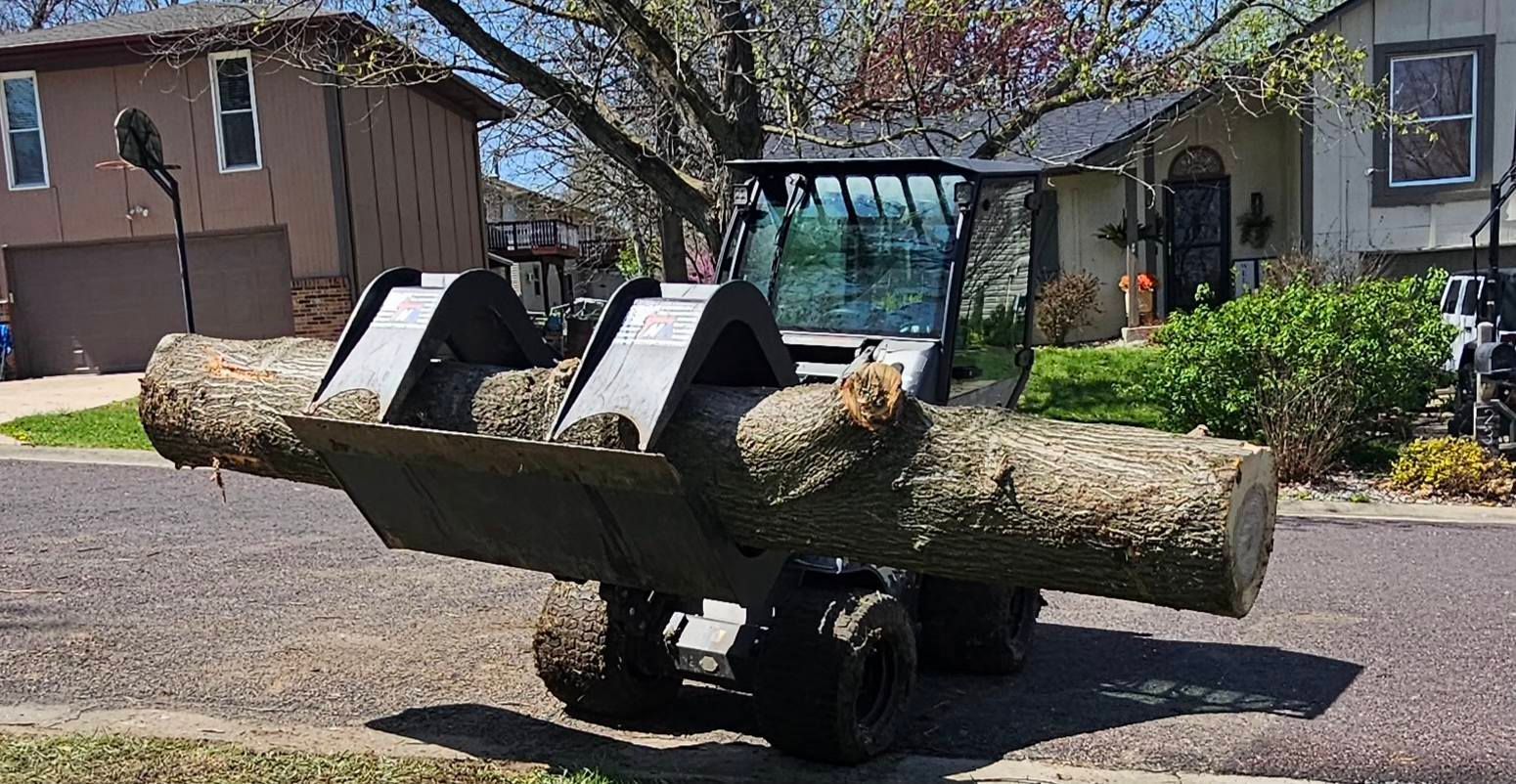 A tractor is carrying a large log in its bucket.