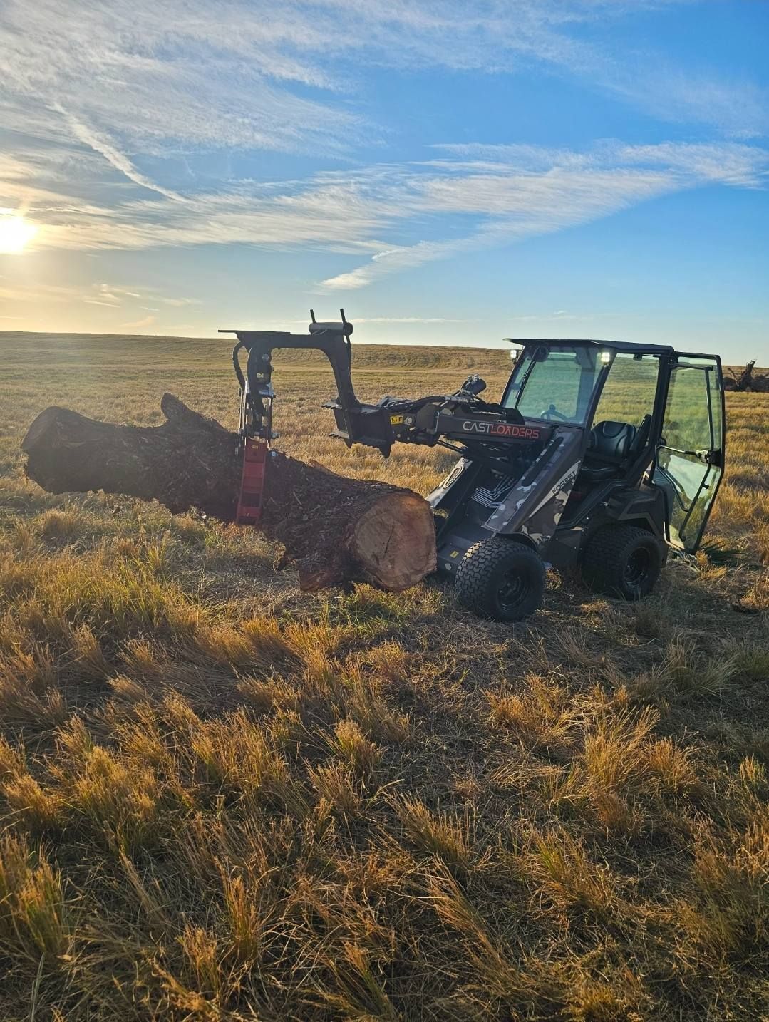A tractor is carrying a large log in a field.