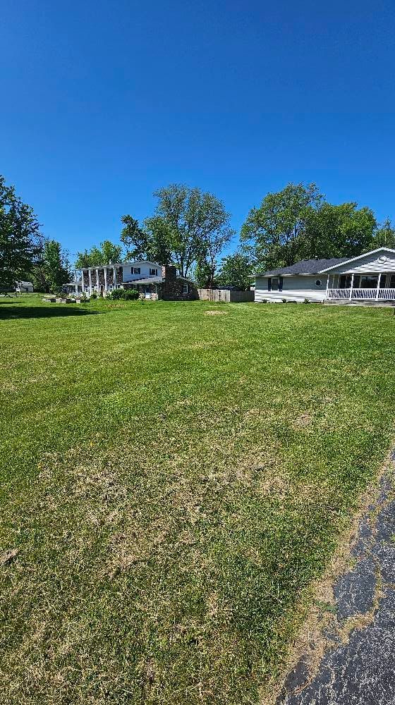 A large lush green field with houses in the background and a blue sky.
