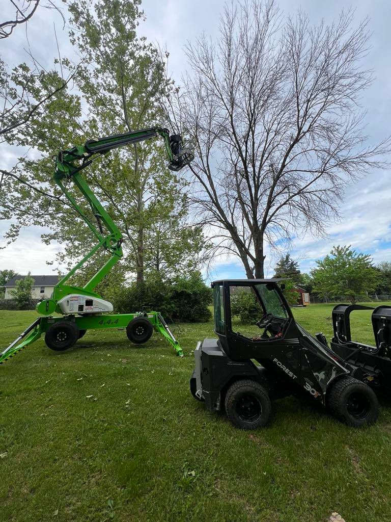 A green crane is sitting next to a black forklift in a grassy field.