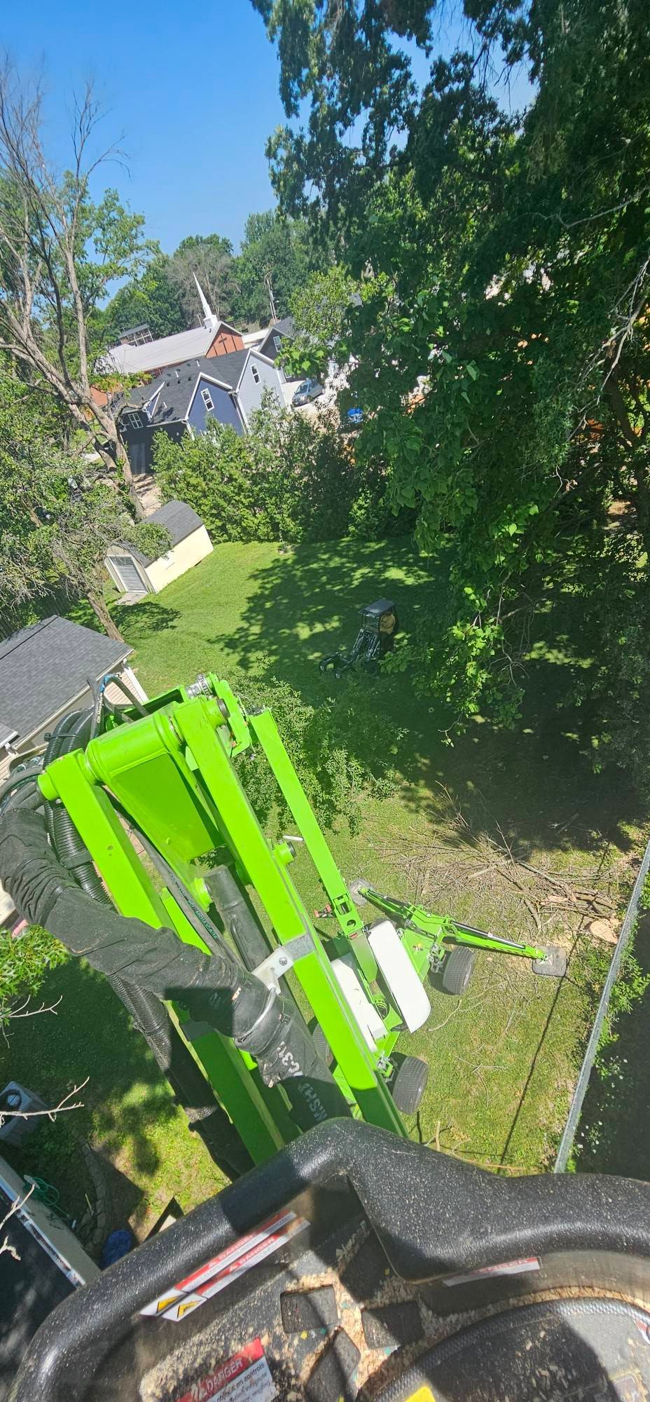 A green tractor is cutting a tree in a yard.