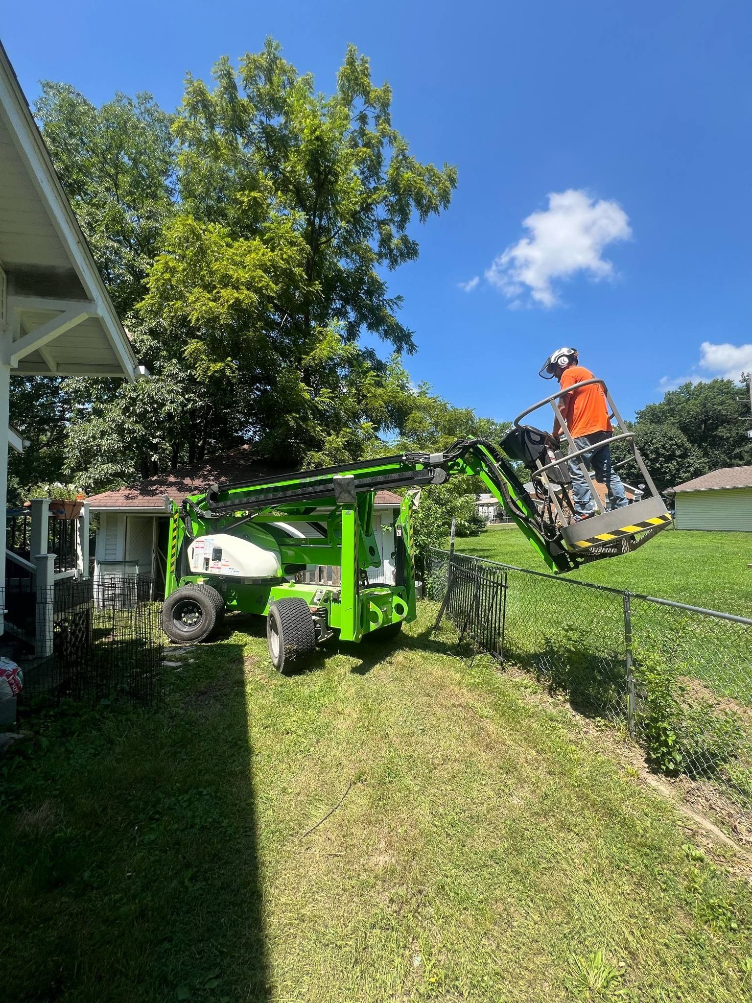 A man is standing in a bucket on a lift cutting a tree.