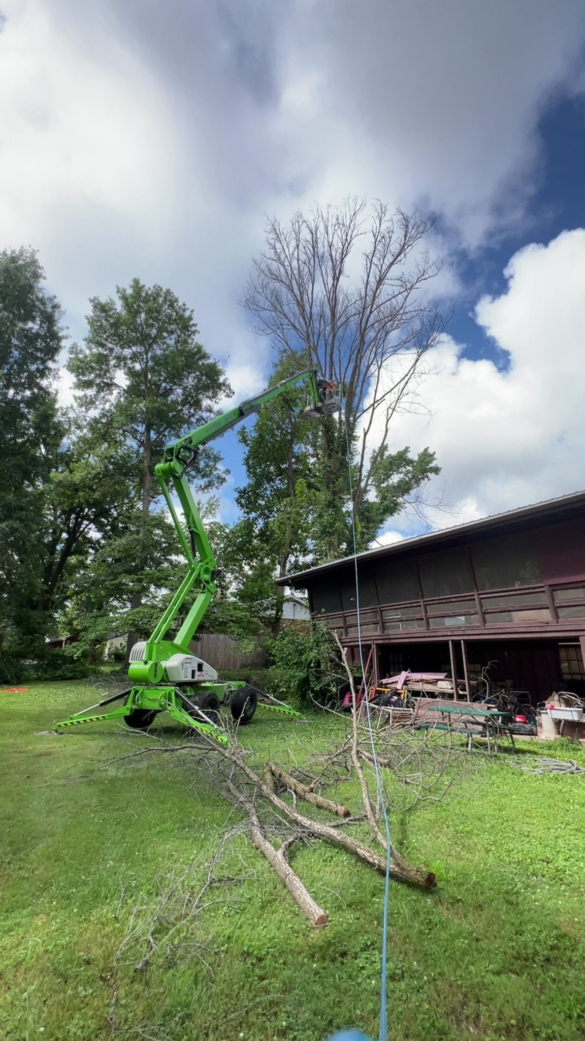 A green crane is cutting a tree in front of a house.