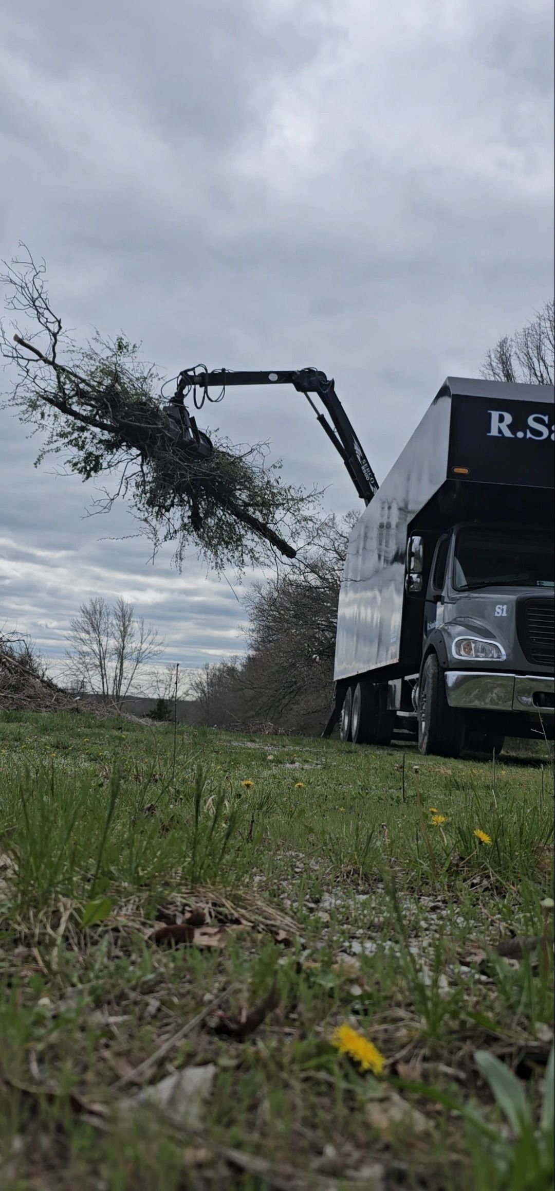 A truck is cutting down a tree in a field.