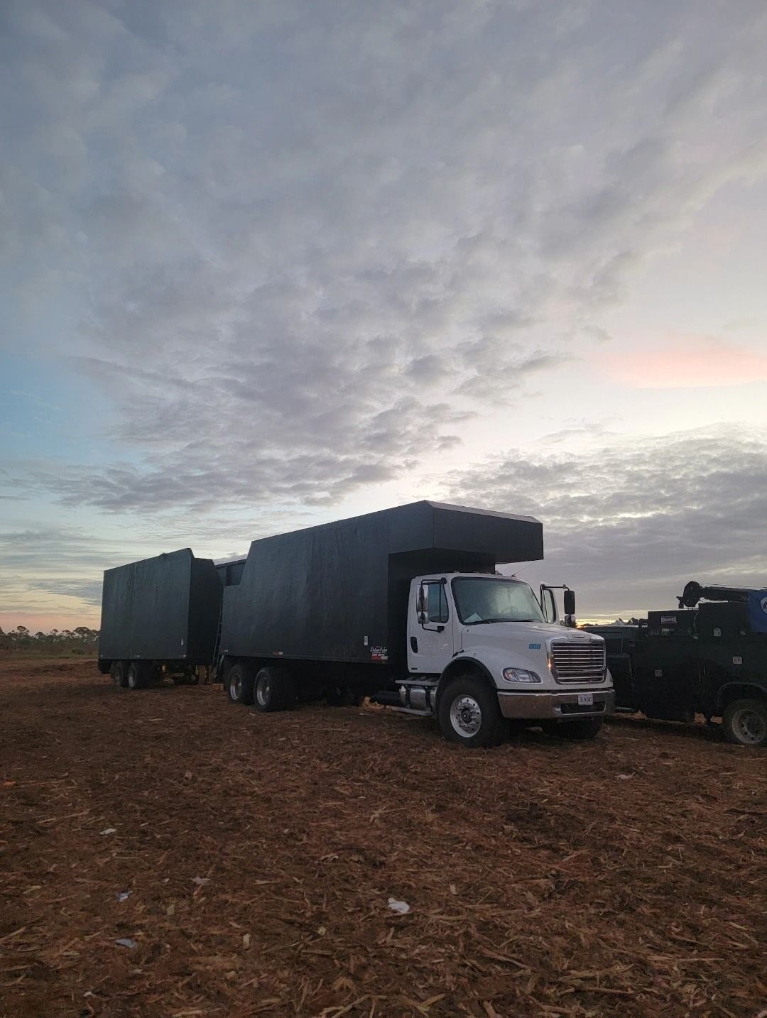 A white truck with a black trailer is parked in a dirt field.