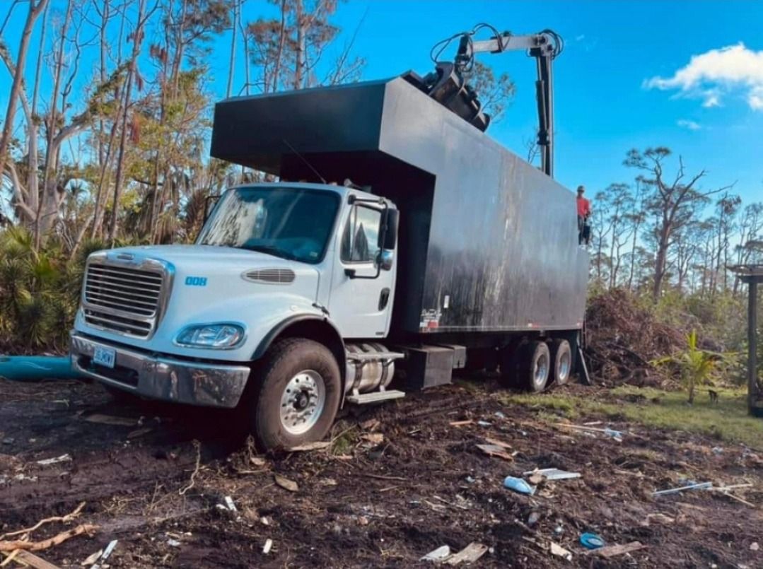 A white truck is parked in a dirt field with trees in the background.