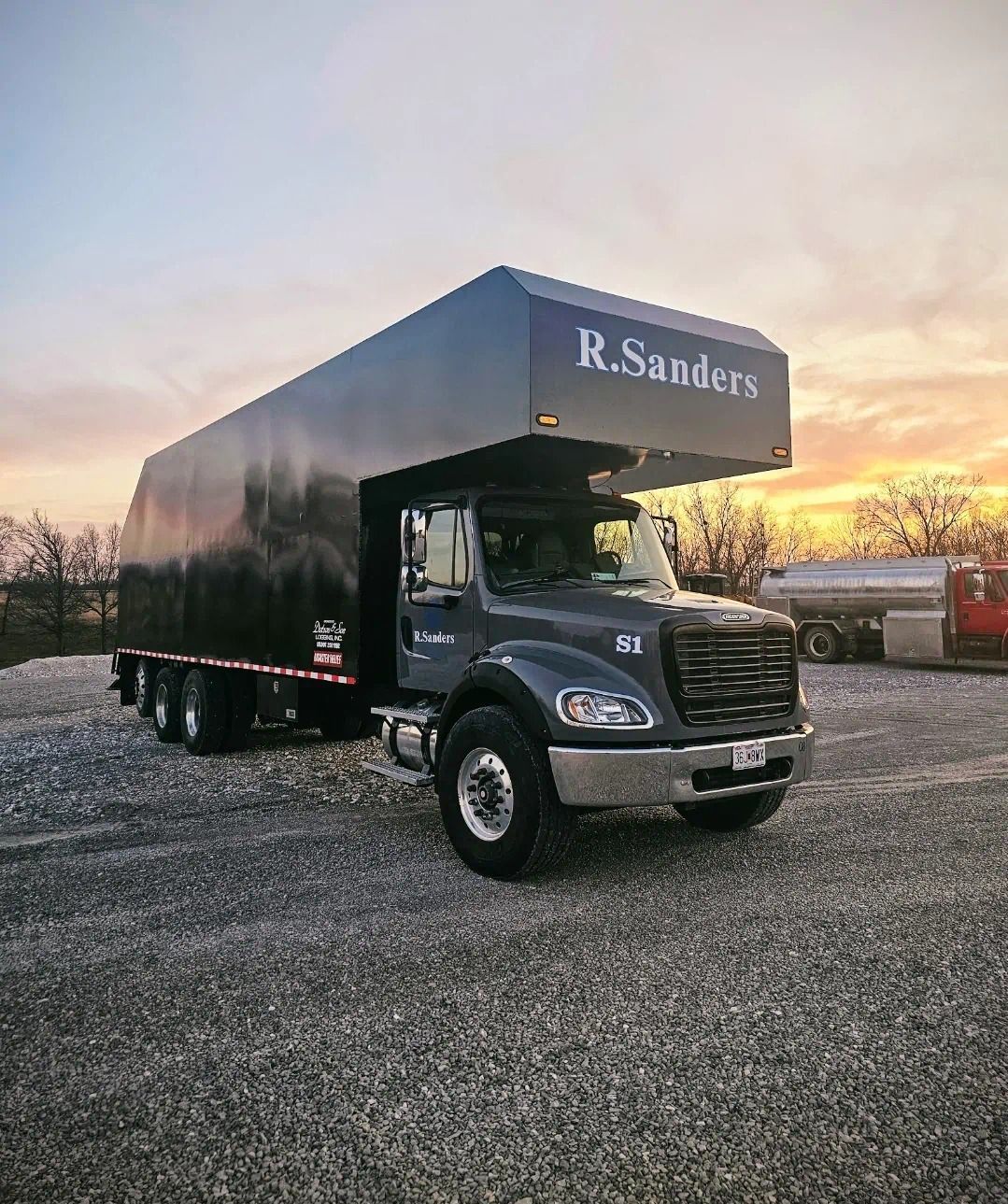 A r. sanders truck is parked in a gravel lot at sunset.