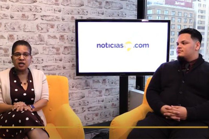 A man and a woman are sitting in front of a tv screen that says noticias.com