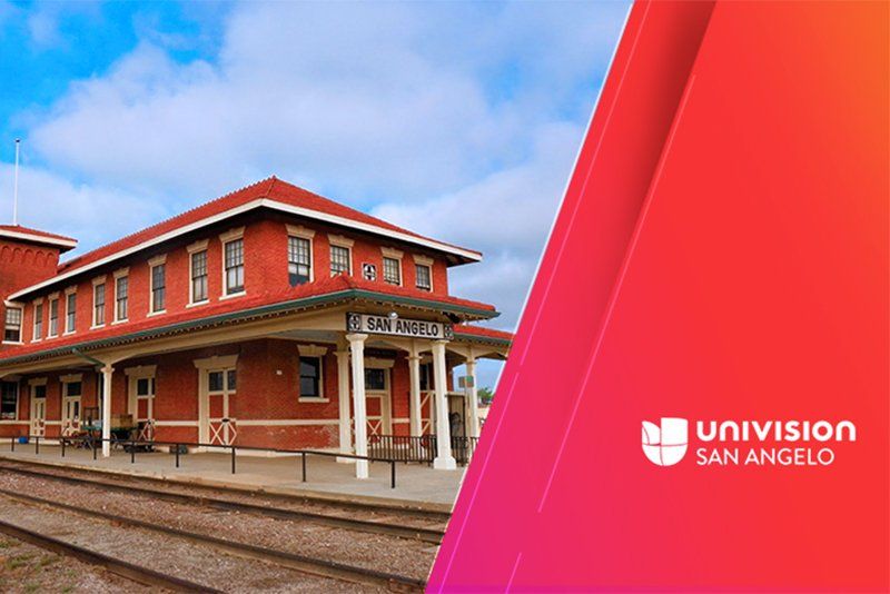 A brick building with a red roof is next to train tracks.