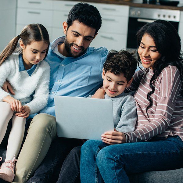 A family is sitting on a couch looking at a laptop.