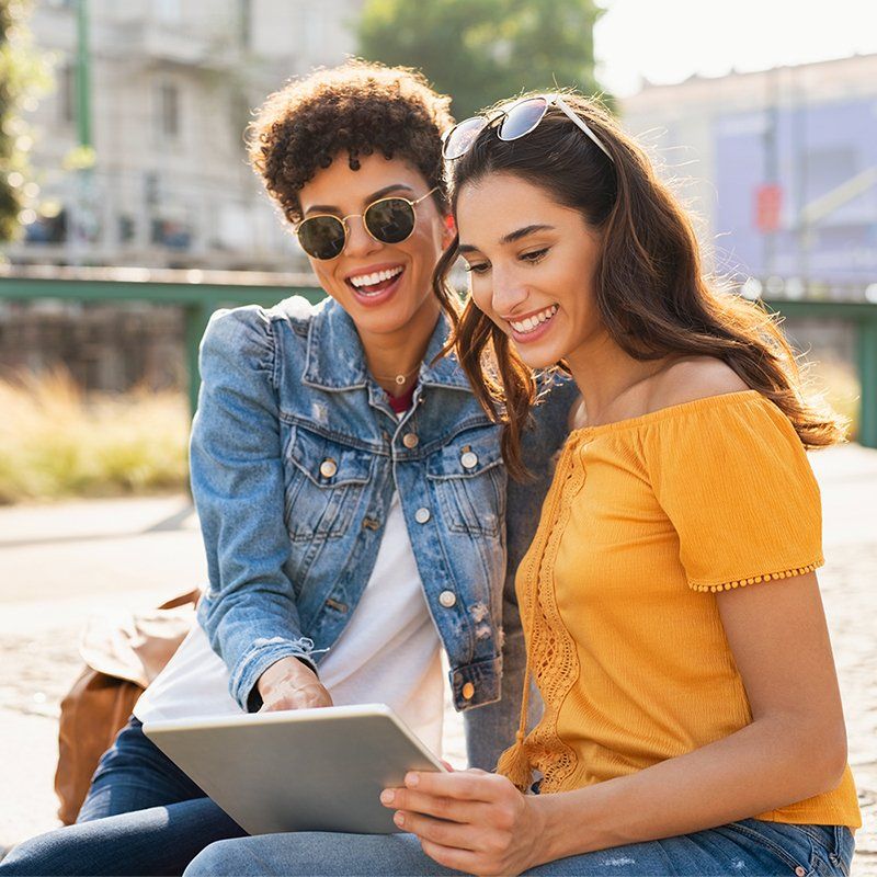 Two women are sitting next to each other looking at a tablet.