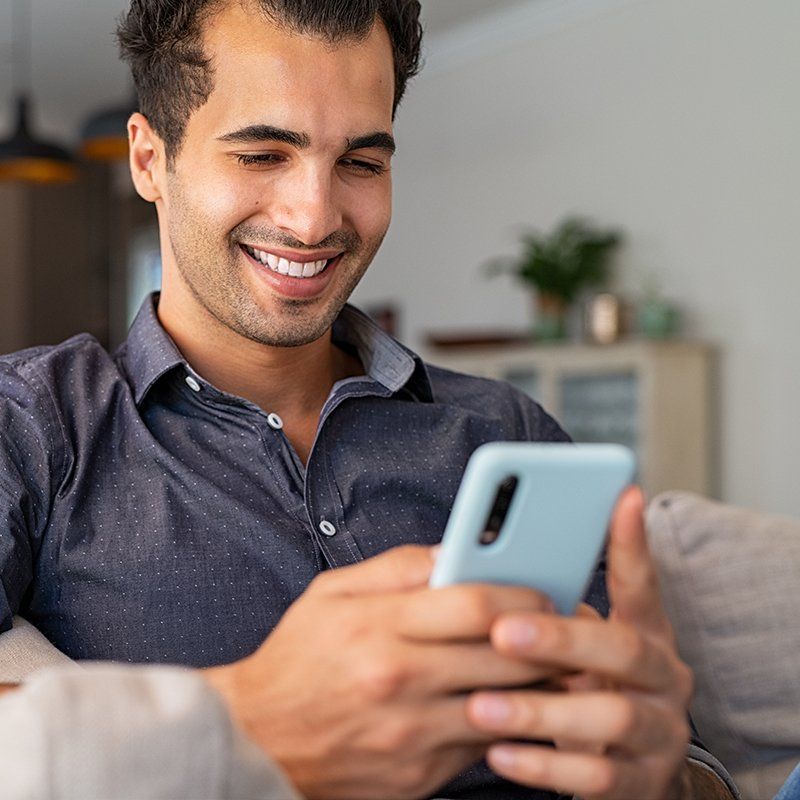 A man is sitting on a couch looking at his cell phone.