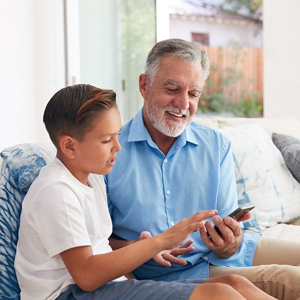 A man and a boy are sitting on a couch looking at a cell phone.