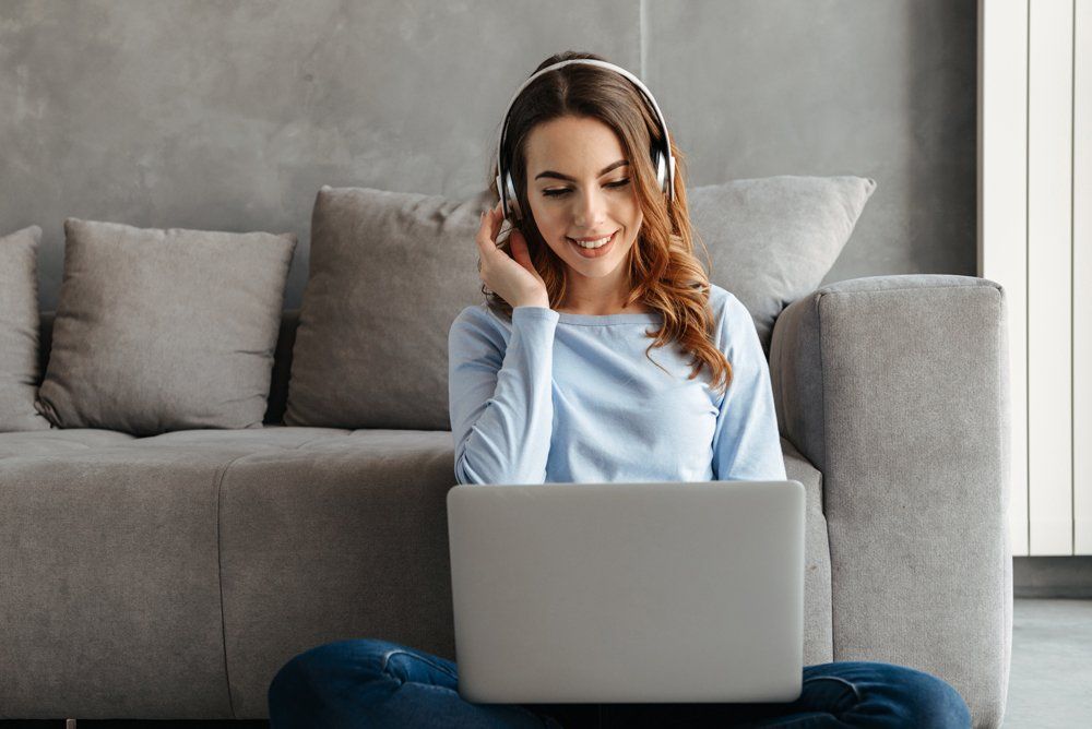 A woman wearing headphones is sitting on the floor using a laptop computer.