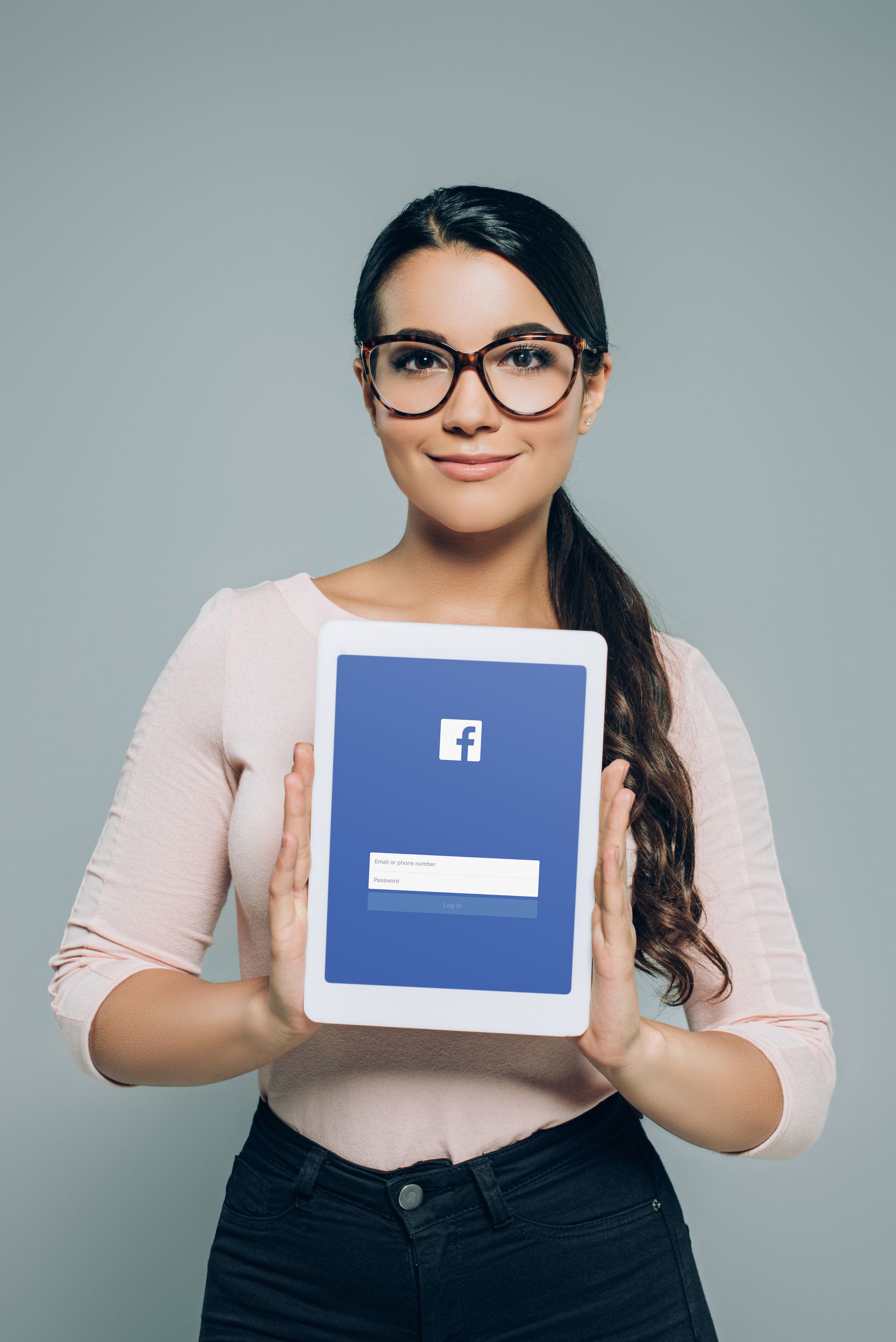Woman with glasses holding a tablet with facebook icon on it