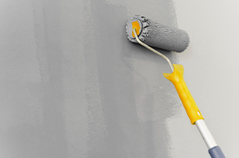 Paint roller applying gray paint to a wall.